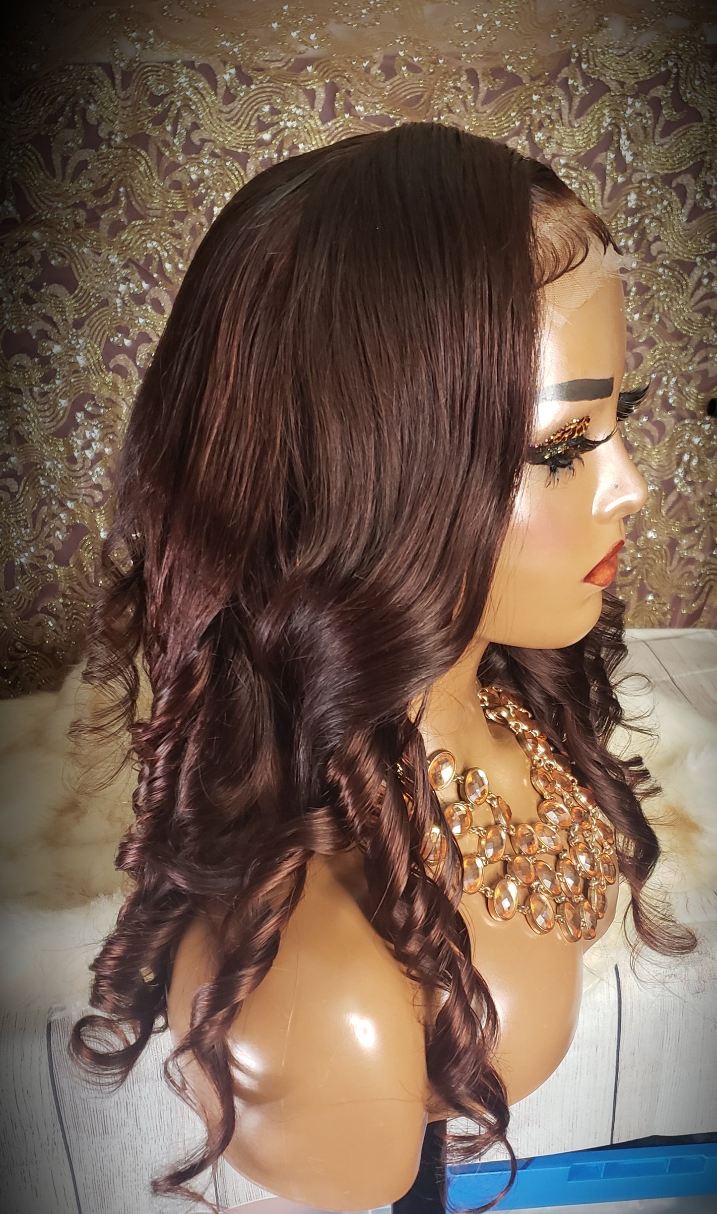 Mannequin head with a brown wig and gold jewelry on a wooden surface.