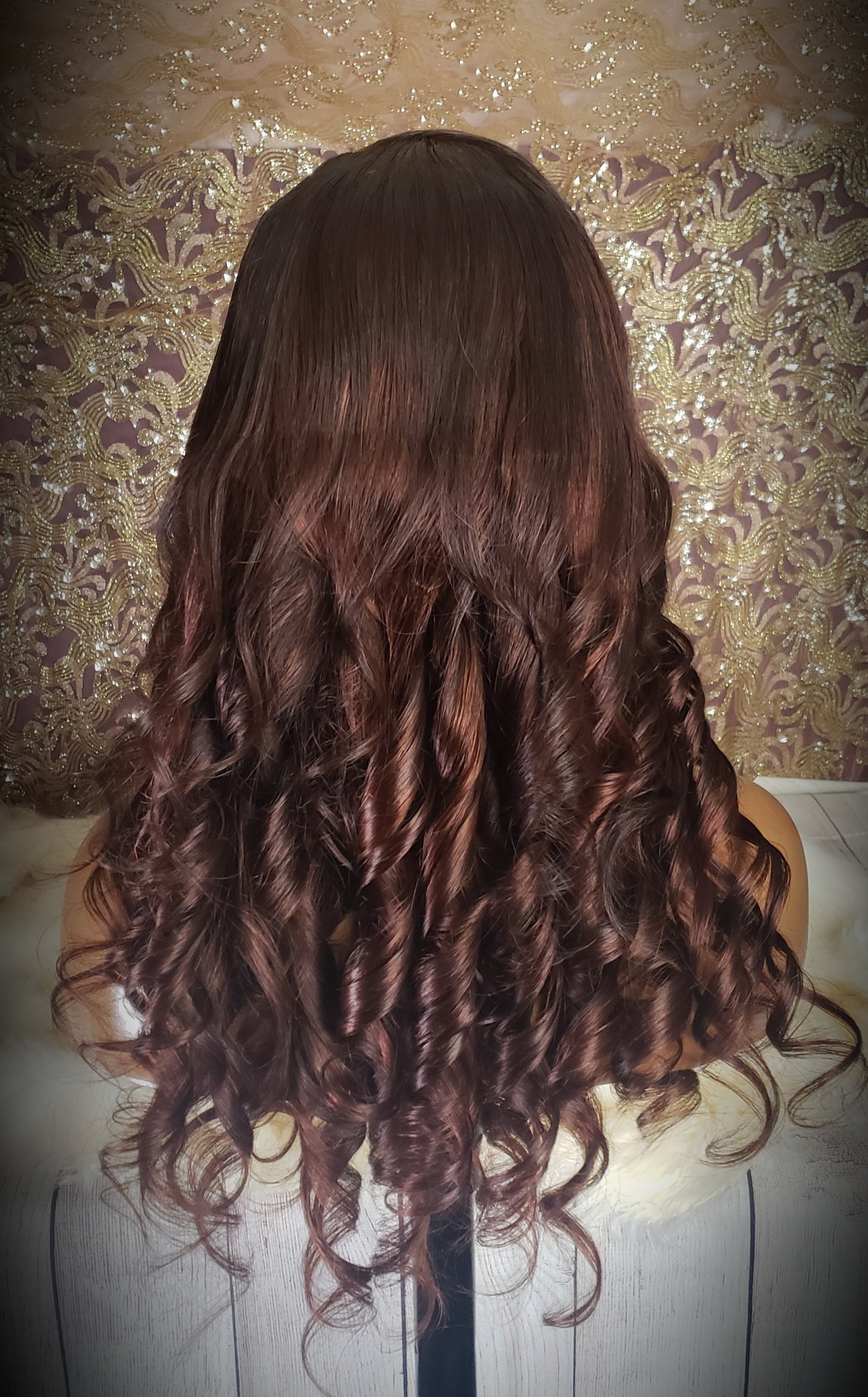 Mannequin head with a brown wig and gold jewelry on a wooden surface.