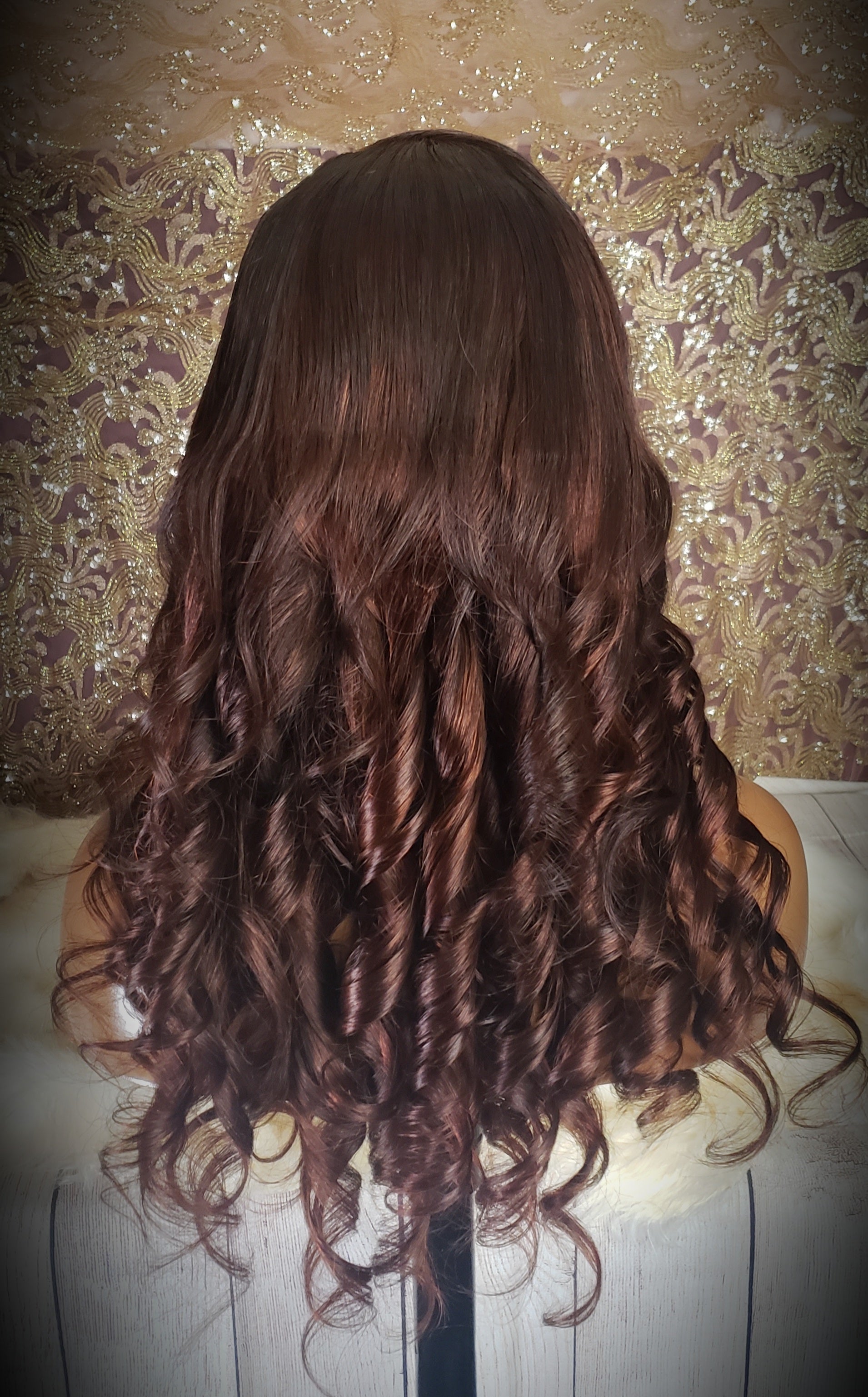 Mannequin head with a brown wig and gold jewelry on a wooden surface.