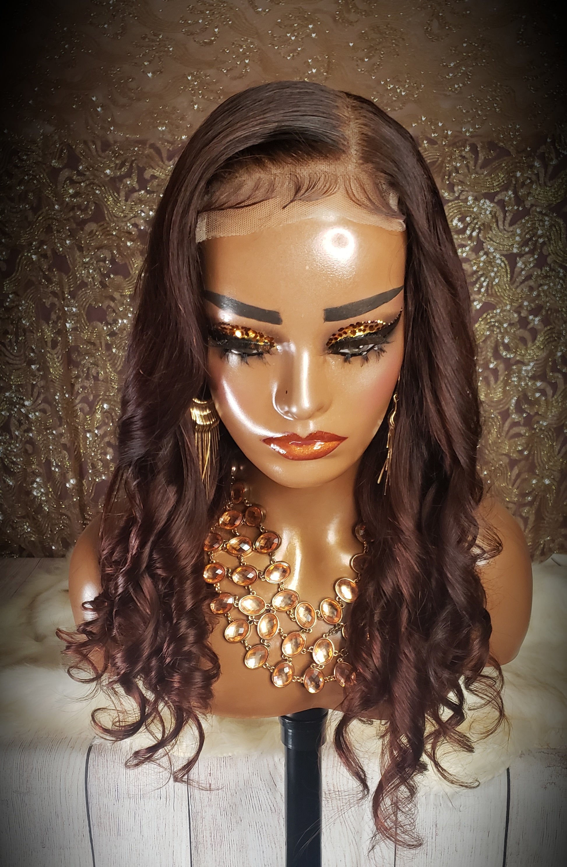 Mannequin head with a brown wig and gold jewelry on a wooden surface.