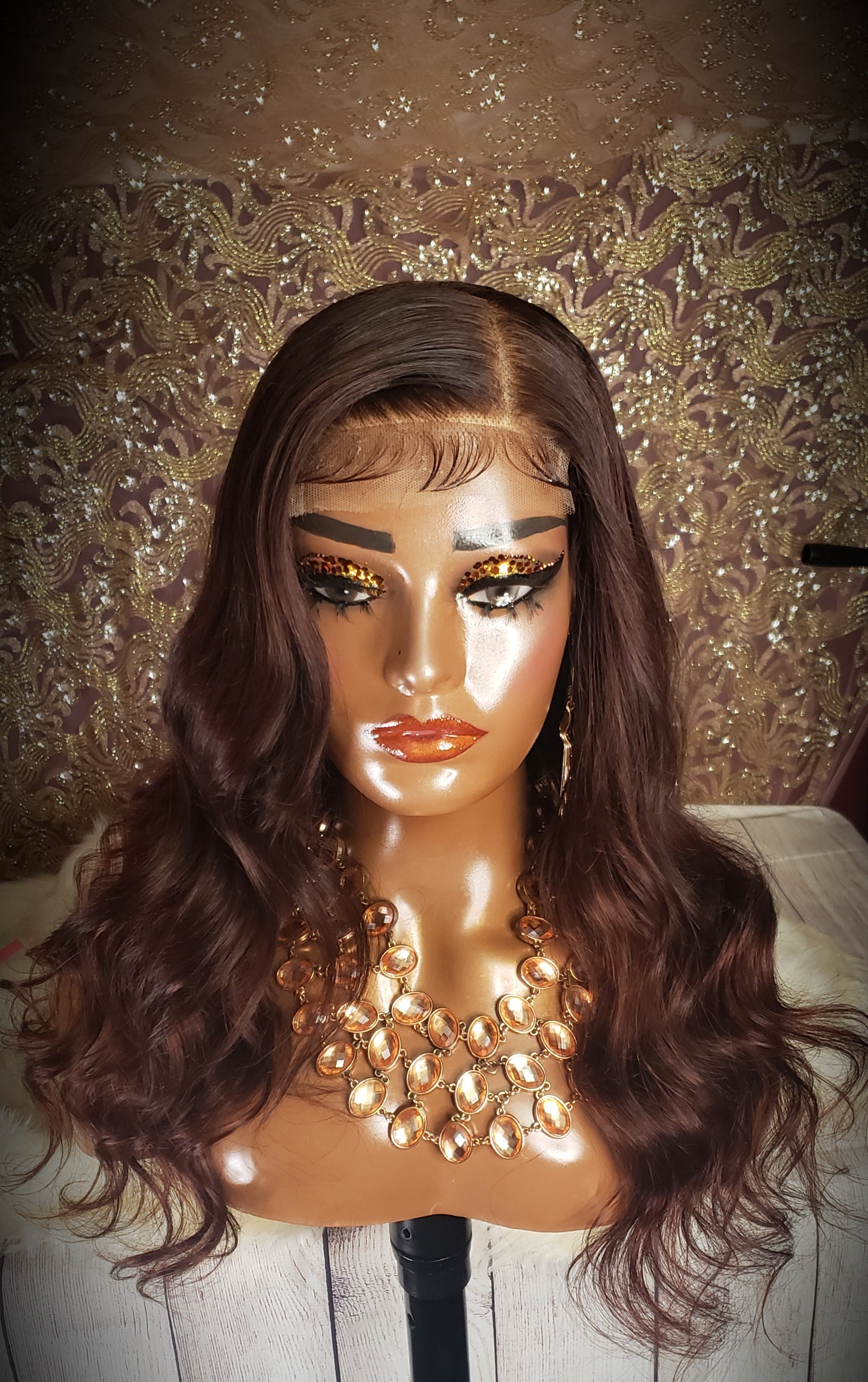 Mannequin head with a brown wig and gold jewelry on a wooden surface.
